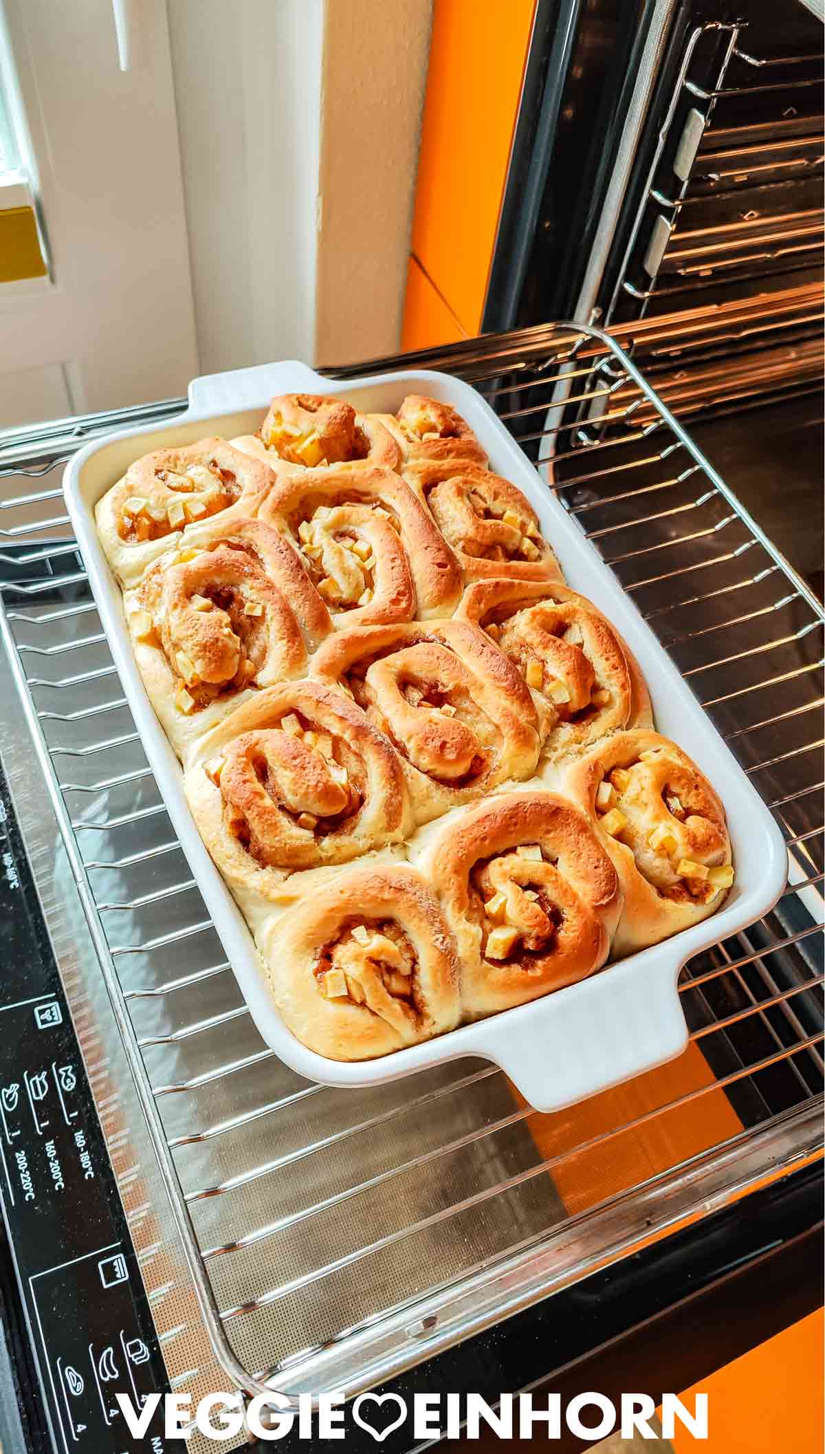 Frisch gebackene Apfel-Zimt-Schnecken in einer weißen Auflaufform im geöffneten Backofen.