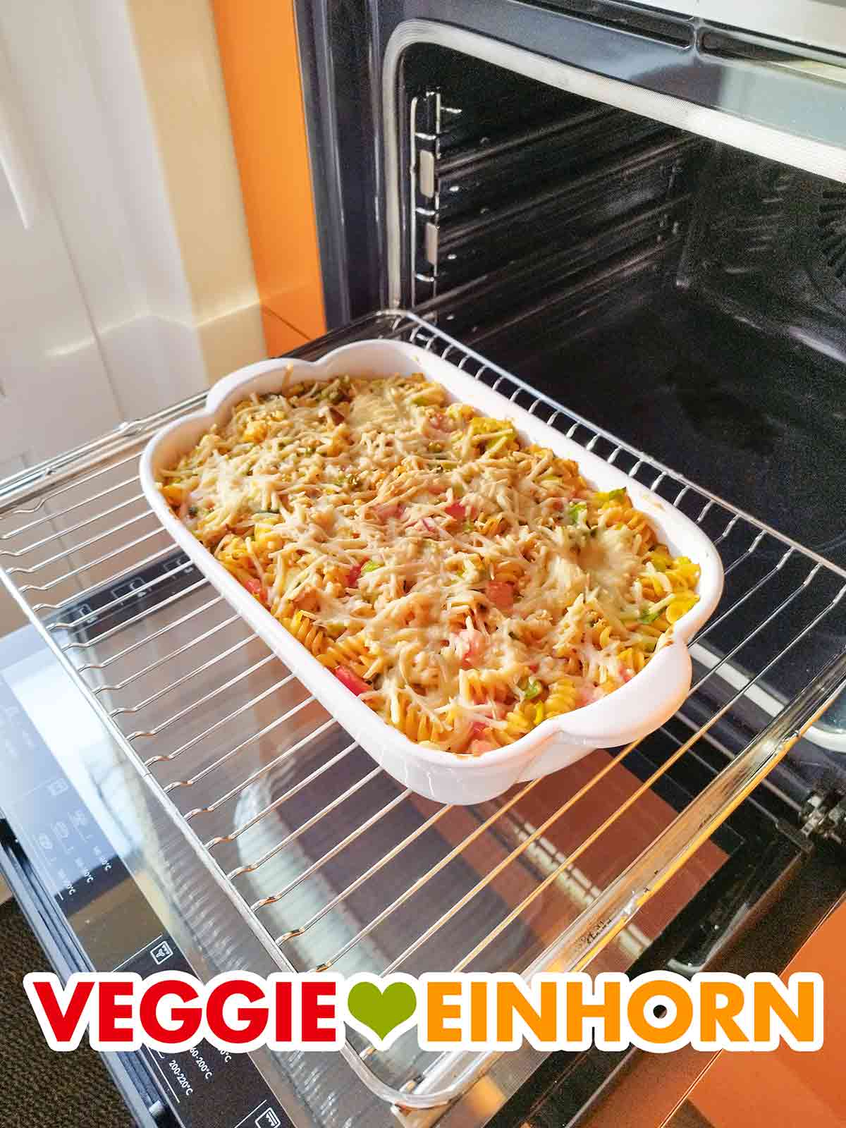 Der mit veganem Käse überbackene Nudelauflauf ist fertig. Fertig gebackener veganer Nudelauflauf mit Räuchertofu, Lauch und Tomaten im geöffneten Ofen