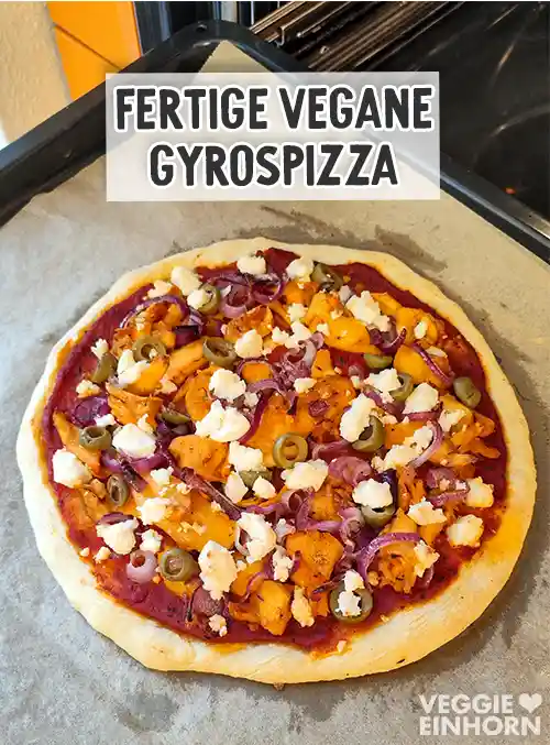 Frisch gebackene vegane Gyrospizza mit Tomatensauce, veganen Gyrosstücken, roten Zwiebeln, Oliven und zerbröckeltem veganem Feta auf einem Backblech.