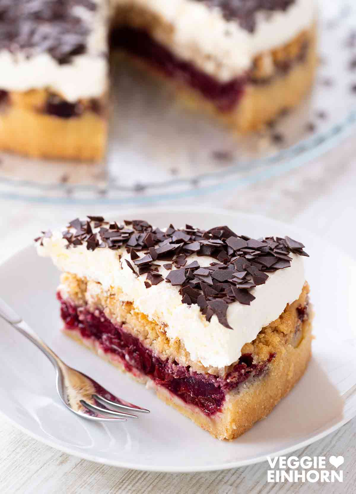 Ein Stück veganer Feuerwehrkuchen auf einem Kuchenteller. Im Hintergrund sieht man den angeschnittenen Kuchen.