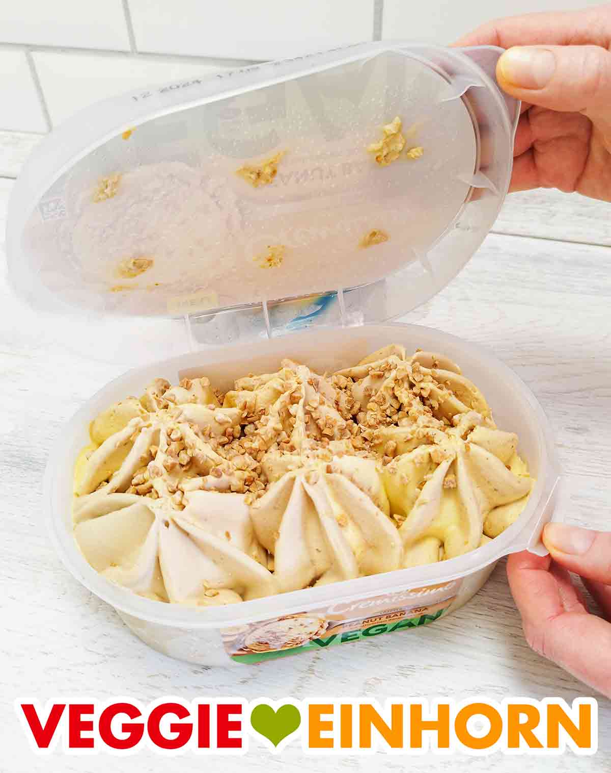 Es ist vegane Erdnusseiscreme und vegane Bananeneiscreme, bestreut mit gehackten, gerösteten Erdnüssen. Geöffnete Packung veganes Cremissimo Peanut Banana Eis