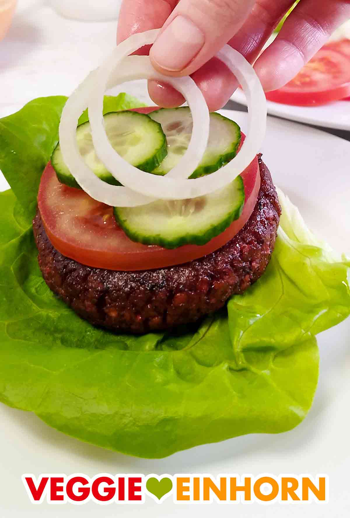 Jetzt kommen noch Gurke und Zwiebel darauf. Gurkenscheiben und Zwiebelringe auf dem veganen Burger