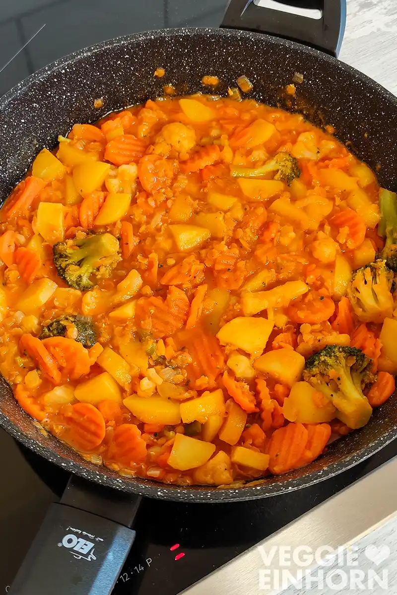 Eine große Pfanne mit veganem Gemüsecurry mit roten Linsen, Kartoffeln und Kokosmilch auf einem Herd.