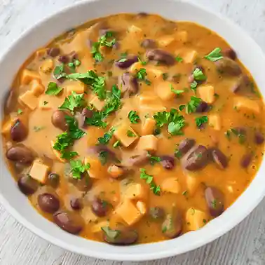Cremiger veganer Kartoffeleintopf mit Kidneybohnen und veganen Fleischwurst-Würfeln, garniert mit frischer Petersilie in einem weißen Teller.