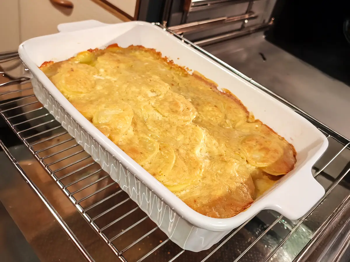 Goldbraun überbackenes veganes Kartoffelgratin in einer weißen Auflaufform auf dem Ofenrost.