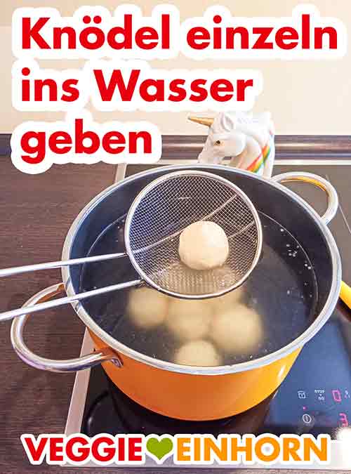 Die Kartoffelklöße einzeln mit einer Schaumkelle ins Kochwasser geben Eine Schaumkelle mit einem Knödel im Topf