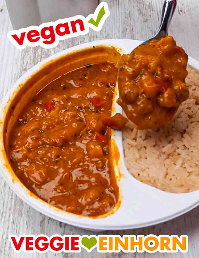 Das vegane Kichererbsencurry passt gut zu dem Reis. Das vegane Kichererbsencurry von Du Darfst wird mit einem Löffel auf den Reis in der Menüschale gefüllt.