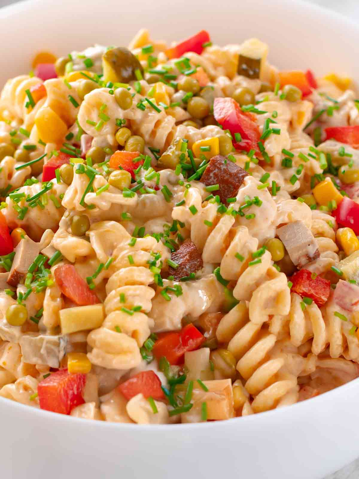 Klassischer veganer Nudelsalat mit Räuchertofu, Mayonnaise, Erbsen, Paprika, Mais und Essiggurken in einer Salatschale, von oben gesehen