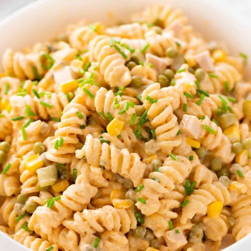 Nahaufnahme einer Schüssel mit cremigem veganem Nudelsalat aus Fusilli, veganer Fleischwurst, Erbsen, Mais und Gewürzgurken, bestreut mit frischem Schnittlauch.