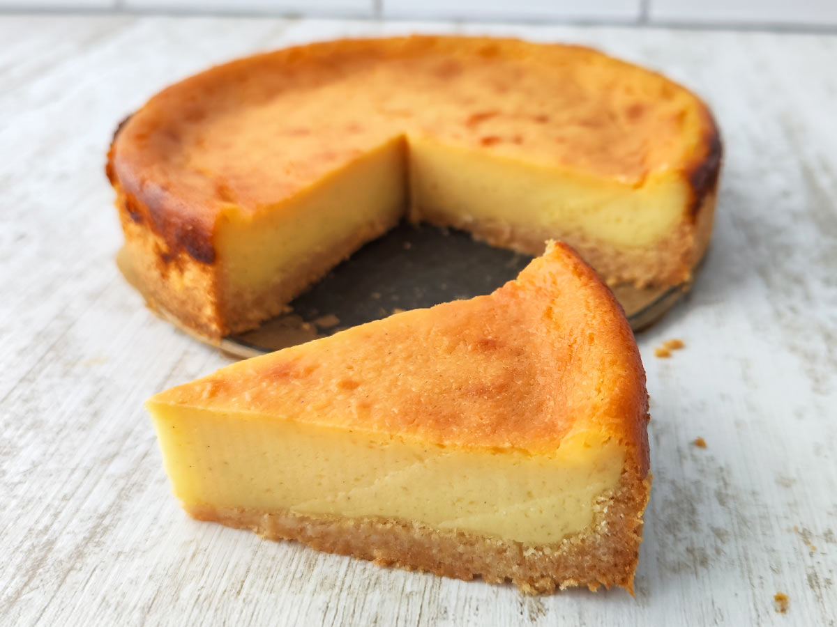 Kleiner veganer Käsekuchen mit goldbrauner Oberfläche, ein Stück ist herausgeschnitten und davor platziert.