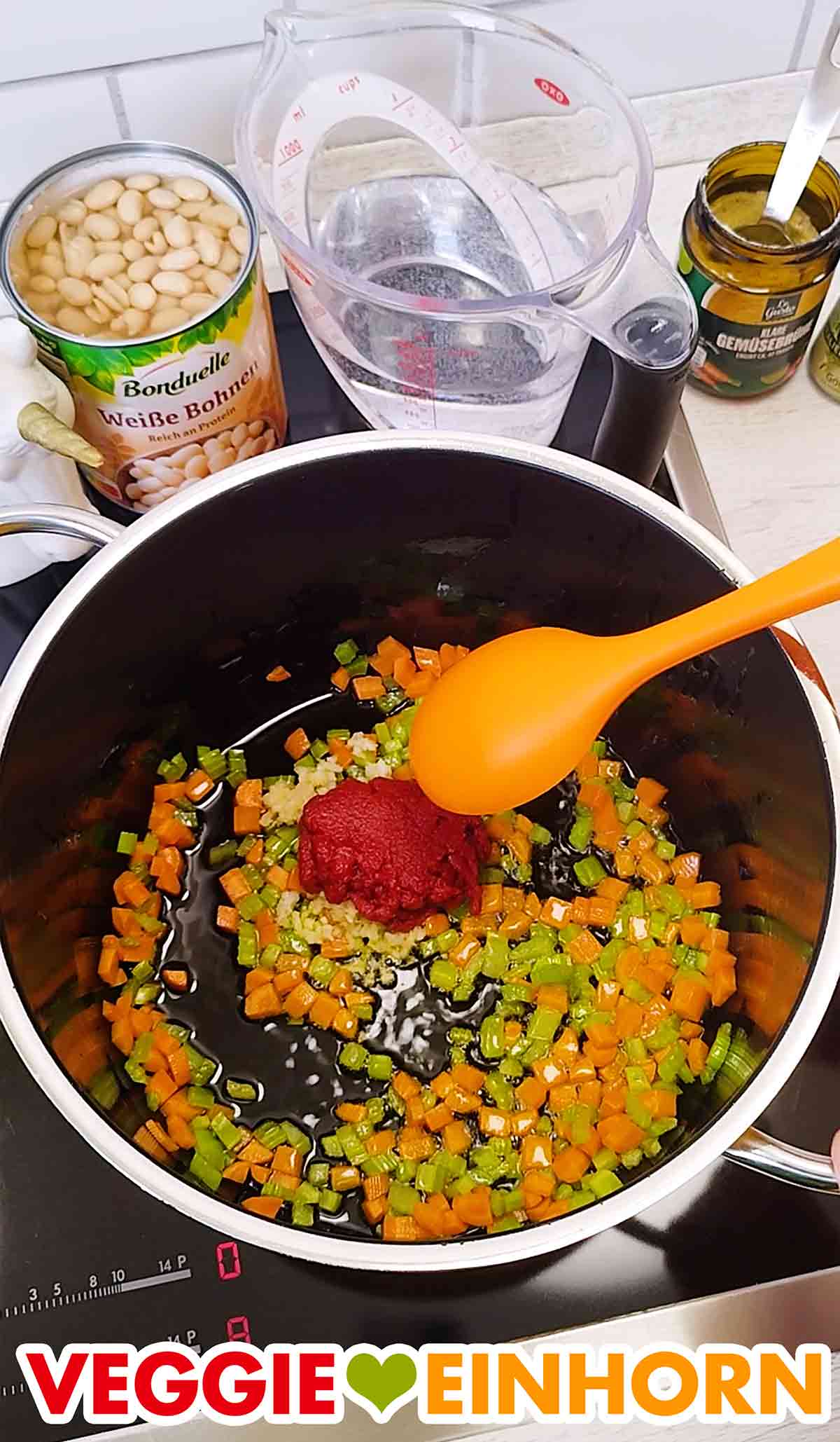 Das Tomatenmark und der gepresste Knoblauch im Topf mit den Möhrenwürfelchen, Stangensellerie und Olivenöl. Knoblauch und Tomatenmark im Topf mit den Möhren und Staudensellerie