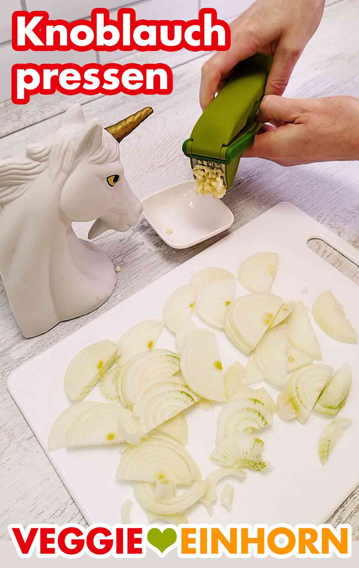 Eine Knoblauchzehe durchpressen. Knoblauch in der Knoblauchpresse und Schneidebrett mit Zwiebeln