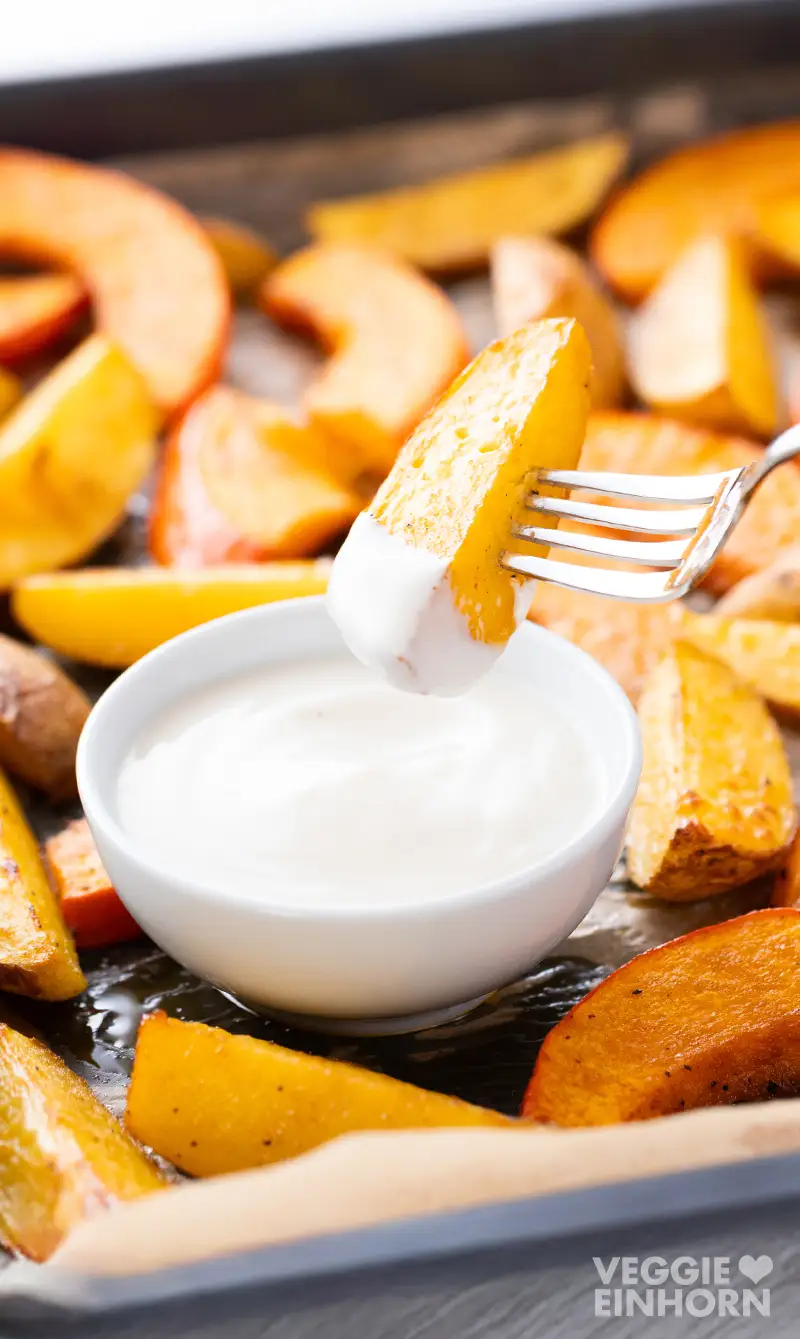 Kartoffelspalte auf einer Gabel über einer Schale mit veganem Tahini-Joghurt-Dressing.