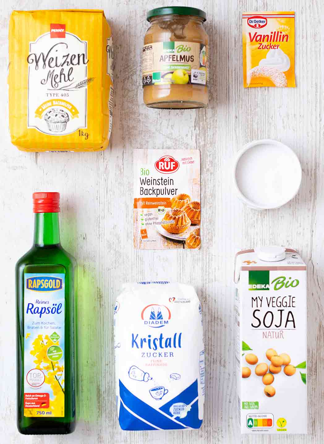 Zutaten für vegane Waffeln auf einem hellen Untergrund: Weizenmehl, Apfelmus, Vanillinzucker, Weinsteinbackpulver, Rapsöl, Zucker und Sojamilch.