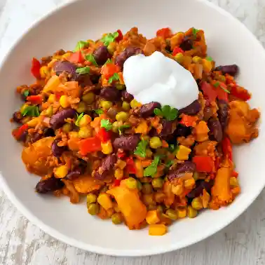 Teller mit bunter veganer Kartoffelpfanne nach mexikanischer Art mit Kidneybohnen, Mais, Erbsen, Paprika und veganem Hack, mit einem Klecks veganer Crème fraîche garniert.