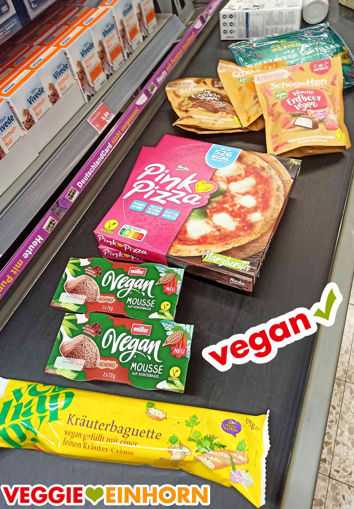 Vegane Lebensmittel einkaufen im Supermarkt Müller Vegan Mousse Schoko, Pink Pizza Margherita, vegane Schogetten und veganes Kräuterbaguette an der Kasse bei Edeka