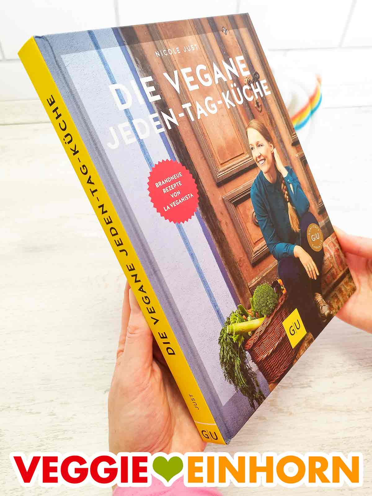 Das Buch Die vegane Jeden-Tag-Küche von La Veganista (Nicole Just). Zwei Hände halten das Buch Die vegane Jeden-Tag-Küche von Nicole Just