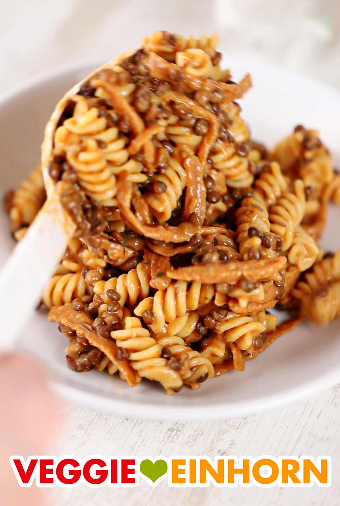 Die Nudeln mit Linsen und veganem Speck werden serviert. Pasta e Lenticchie wird mit einem Servierlöffel auf einen Teller gefüllt