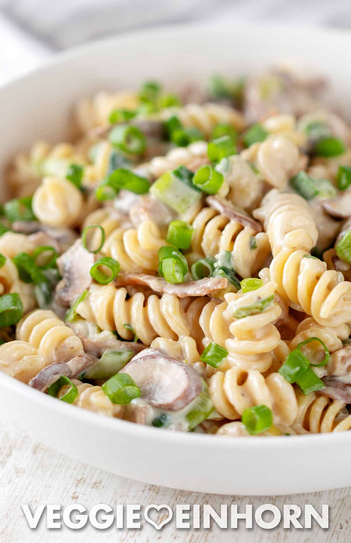 Ein schnelles veganes Nudelgericht mit veganem Speck, Pilzen und Lauchzwiebeln Nahaufnahme von Nudeln mit veganem Speck, Champignons und Frühlingszwiebeln