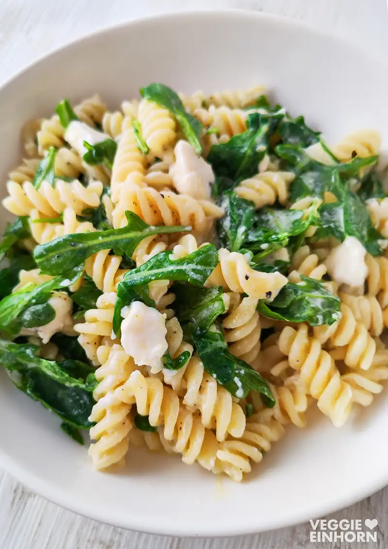Nahaufnahme von Fusilli mit Rucola und veganem Feta in einem weißen Teller.
