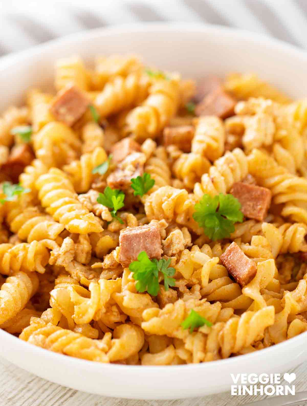 Vegane Leberkäse-Nudeln auf einem weißen Teller, mit gebratenen Stücken von veganem Leberkäse und frischer Petersilie.