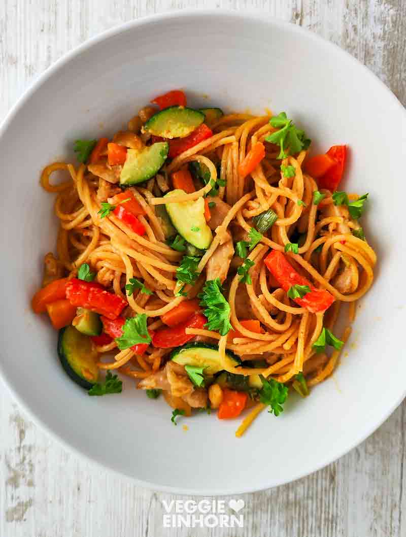 Vegane Nudelpfanne mit Erdnusssoße, Gemüse und veganem Hähnchen in einer weißen Schüssel, dekoriert mit Petersilie.
