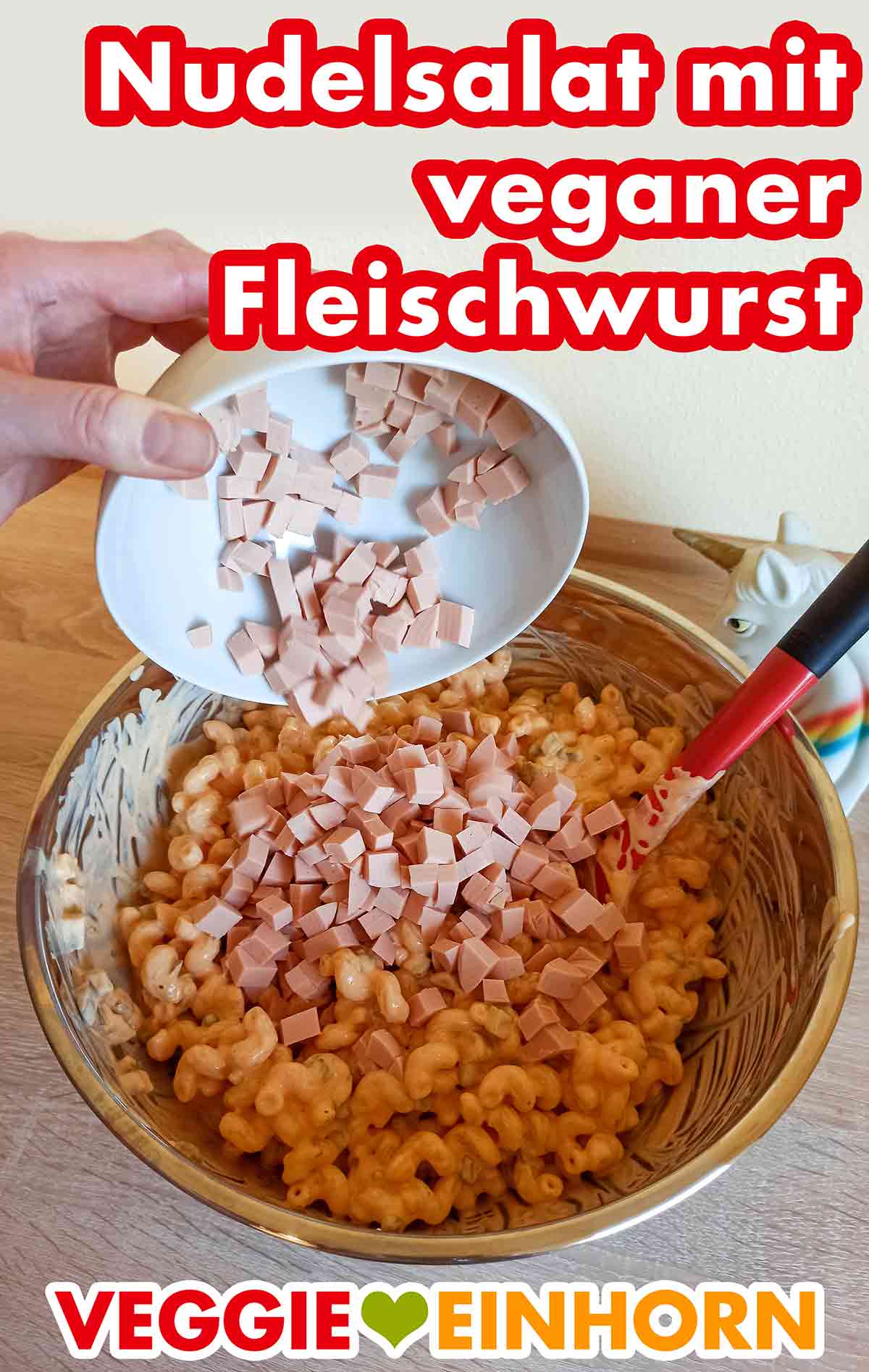 Der Nudelsalat mit veganer Fleischwurst schmeckt fantastisch. Vegane Fleischwurst Würfel werden in eine Schüssel mit Nudelsalat gegeben.