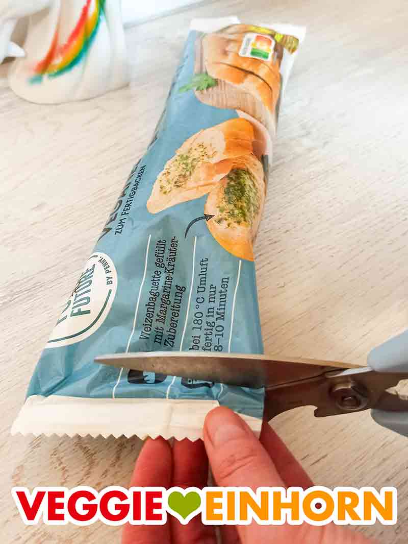 Die Packung des veganen Kräuterbaguettes von Food For Future wird mit der Schere aufgeschnitten. Eine Packung veganes Kräuterbaguette von Penny und eine Schere