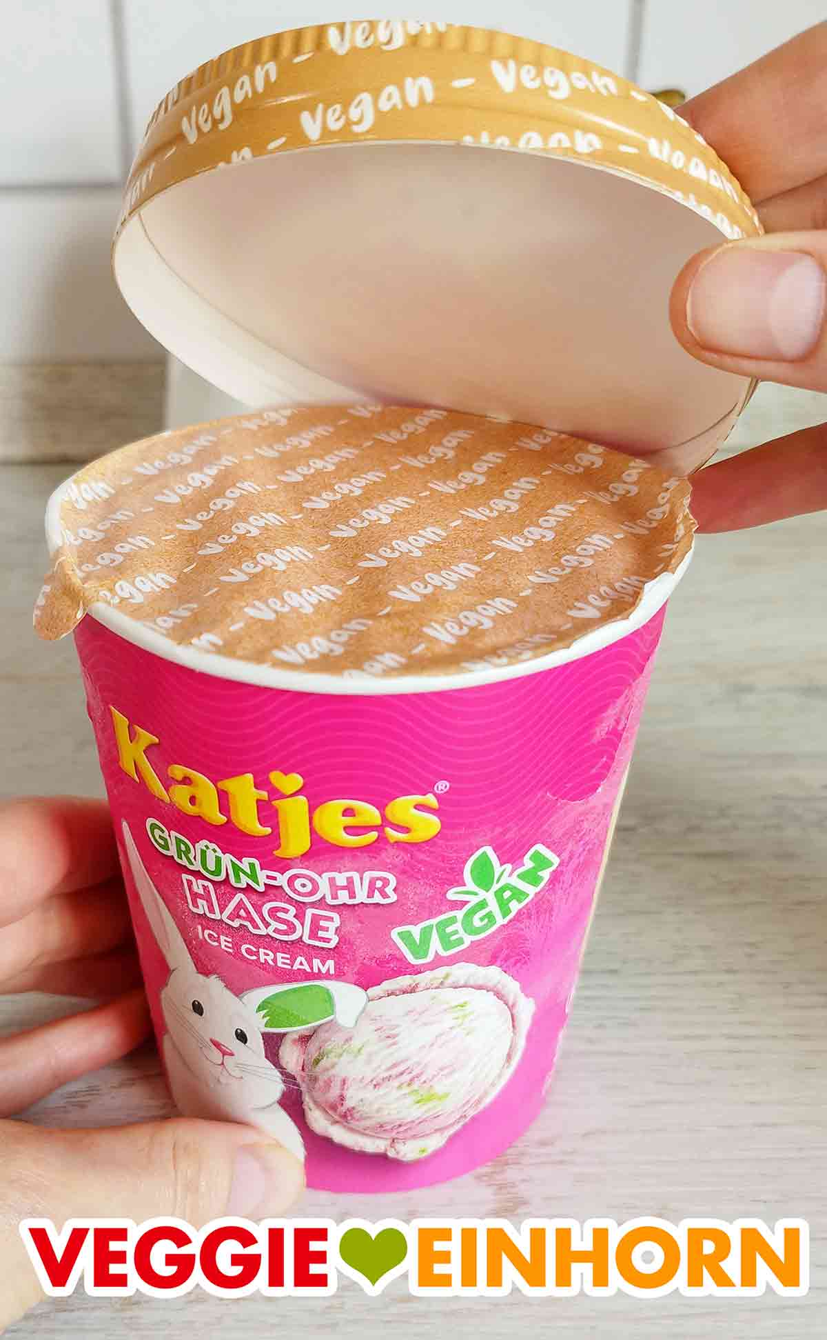 Der Becher Katjes Grünohrhasen Eiscreme wird geöffnet. Der Deckel des Bechers des Katjes Grün Ohr Hasen Eis wird abgehoben.