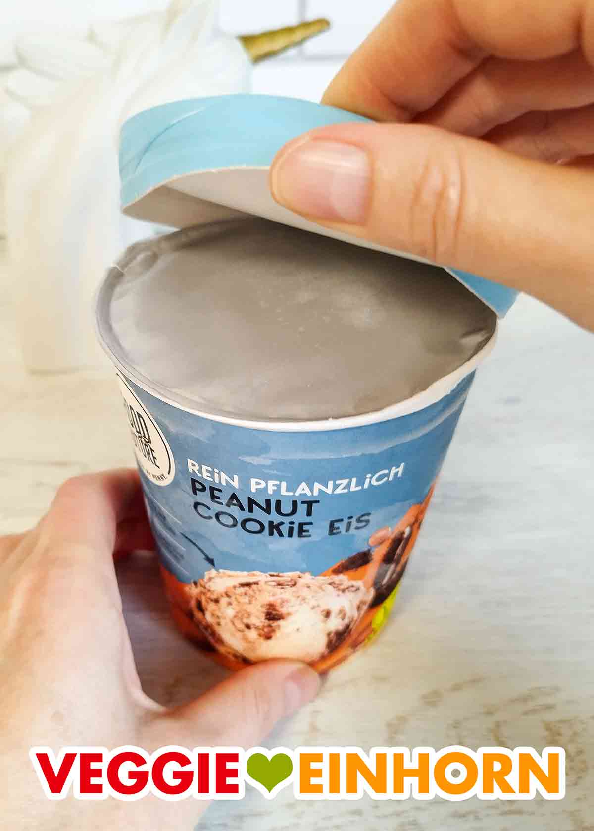 Öffnen des veganen Peanut Cookie Eis von Food for Future. Der Deckel des Bechers Peanut Cookie Eis von Penny wird abgehoben.