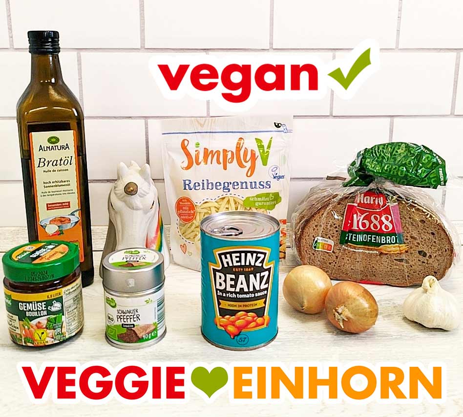 Alnatura Bratöl, Simply V Reibegenuss, Harry 1688 Steinofenbrot, Knorr Gemüse Bouillon, Aldi Gut Bio Schwarzer Pfeffer, Heinz Beanz, Zwiebeln, Knoblauchknolle Bratöl, veganer geriebener Käse, Graubrot, Gemüsebrühe Pulver, Pfeffer, eine Dose Baked Beans, Zwiebeln, Knoblauch