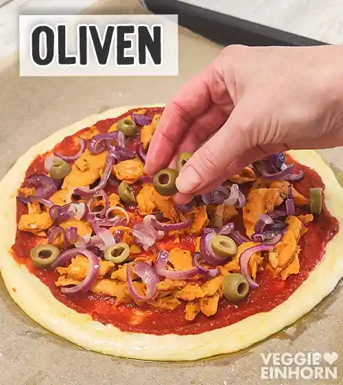 Pizza mit Tomatensauce, veganem Gyros und gebratenen Zwiebeln, die mit grünen Olivenscheiben belegt wird.