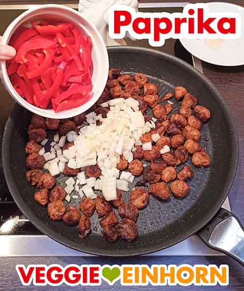Rote Paprika wird in die Pfanne zugefügt Zufügen der Paprika für das vegetarische Gulasch