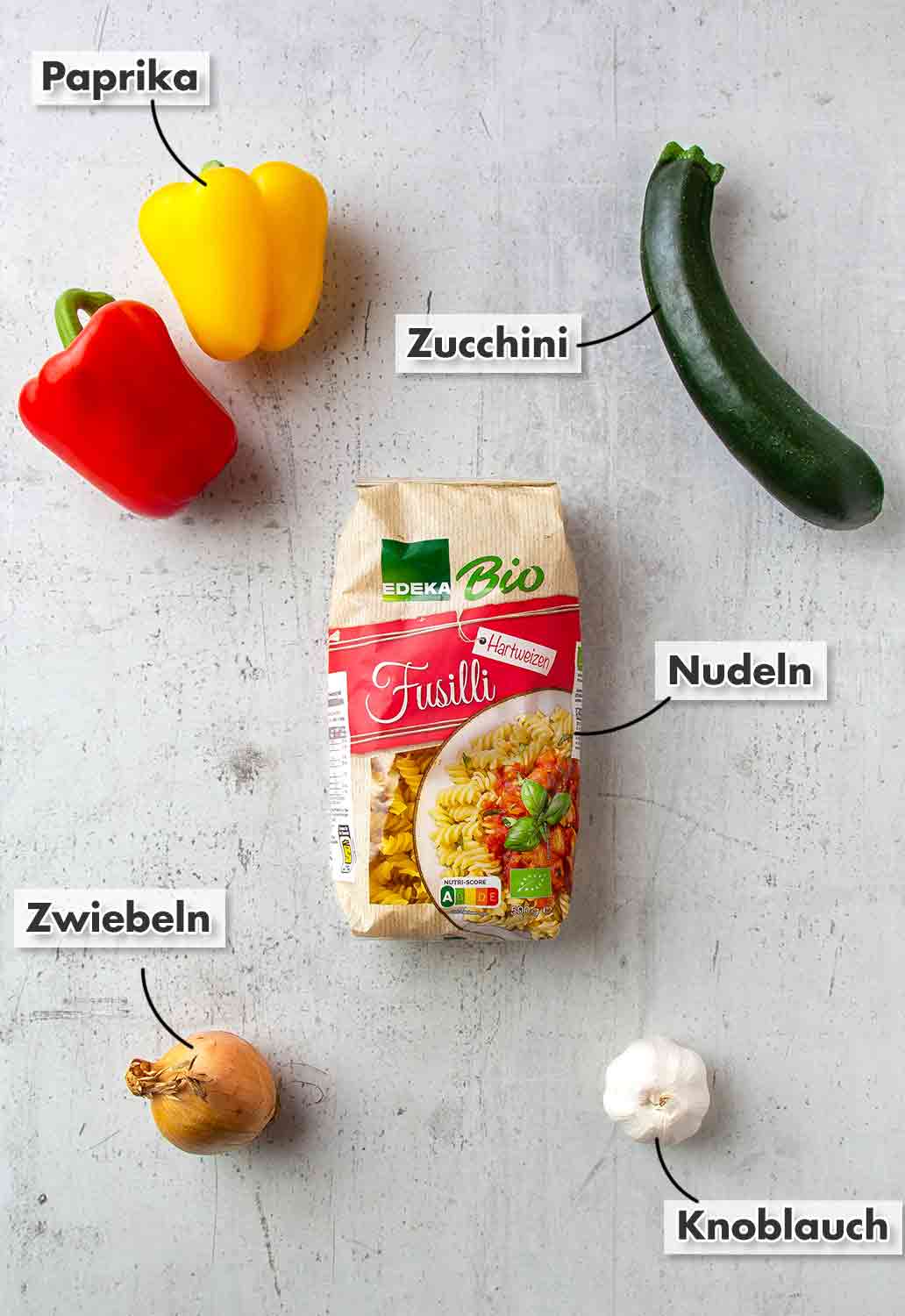 Paprikaschoten, Zucchini, Edeka Bio Fusilli, Zwiebel, Knoblauch Eine rote und eine gelbe Paprika, Zucchini, Nudeln, Zwiebeln, Knoblauch