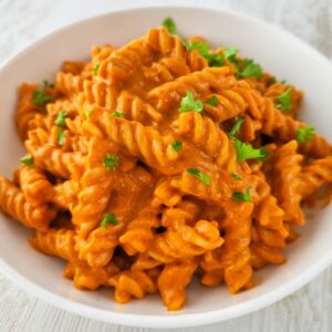 Weißer Teller mit Fusilli mit Gemüsesoße, bestreut mit gehackter Petersilie.