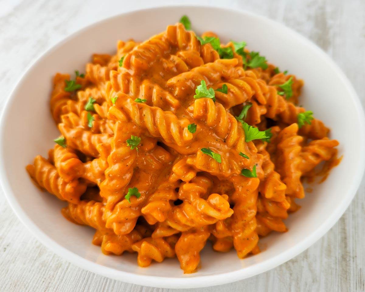Weißer Teller mit Fusilli mit Gemüsesoße, bestreut mit gehackter Petersilie.