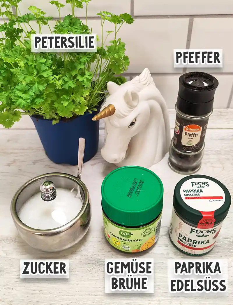Petersilie im Topf sowie Pfeffer, Zucker, Gemüsebrühe und Paprika edelsüß stehen auf einer hellen Küchenfläche.