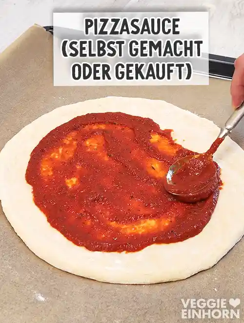 Ein runder Pizzateig auf einem Backblech wird mit roter Pizzasauce bestrichen.