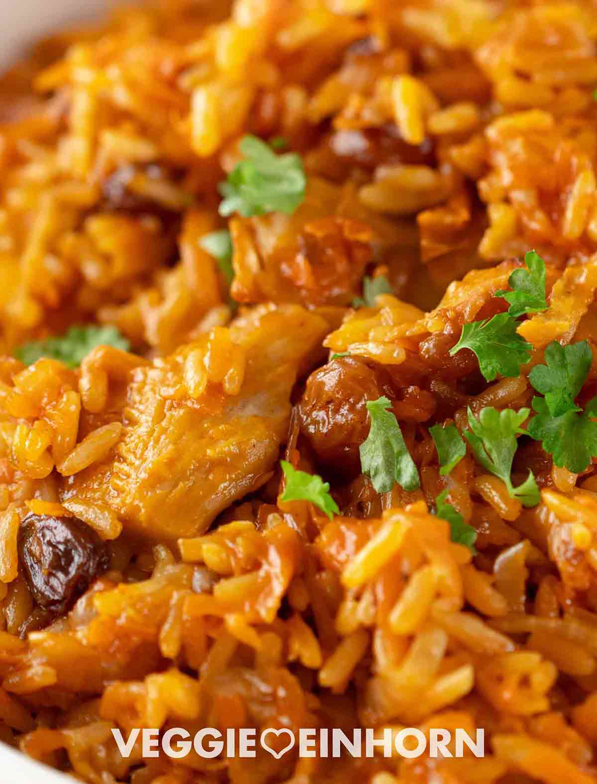 Nahaufnahme eines veganen Plov-Gerichts mit Reis, Karotten, Rosinen und pflanzlichem Fleischersatz, garniert mit frischer Petersilie.