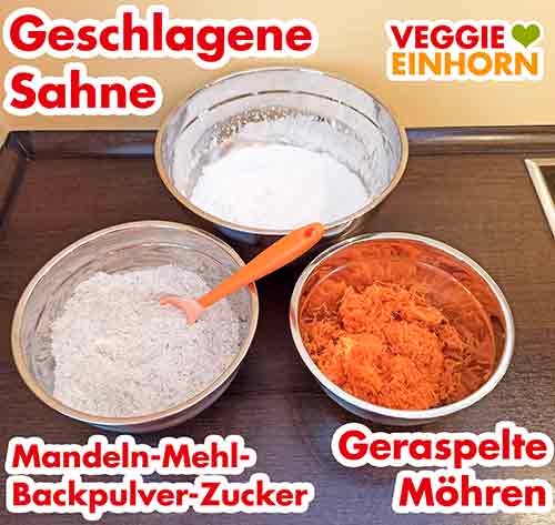 Geschlagene Sahne, trockene Zutaten und Möhrenraspel für den Kuchenteig Drei Rührschüsseln mit den vorbereiteten Zutaten für den Teig