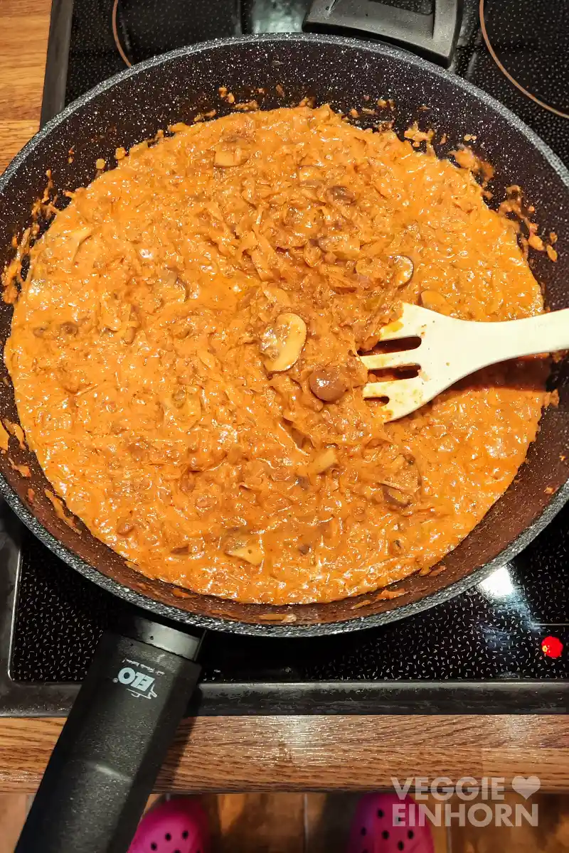 Sauerkrautpfanne mit veganem Hack und Pilzen auf dem Herd, darin rührt ein Pfannenwender.