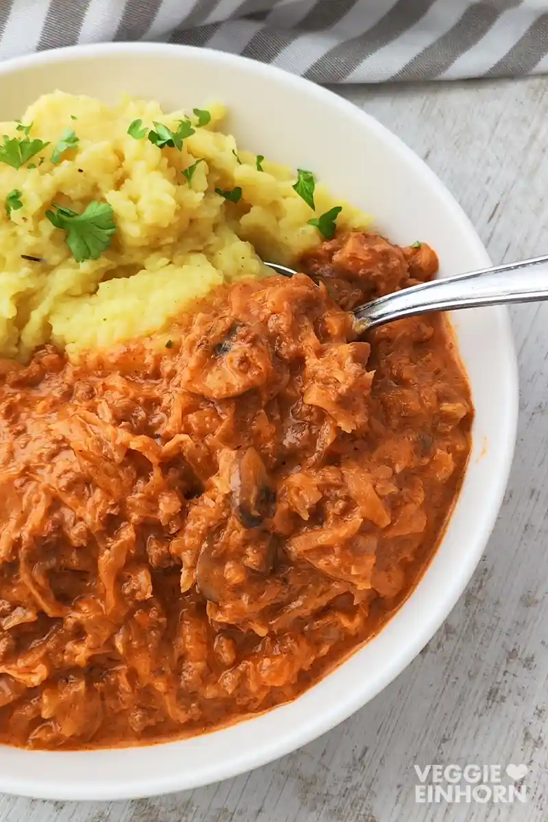 Ein Teller mit veganer Sauerkrautpfanne und Kartoffelpüree, ein Esslöffel steckt darin.