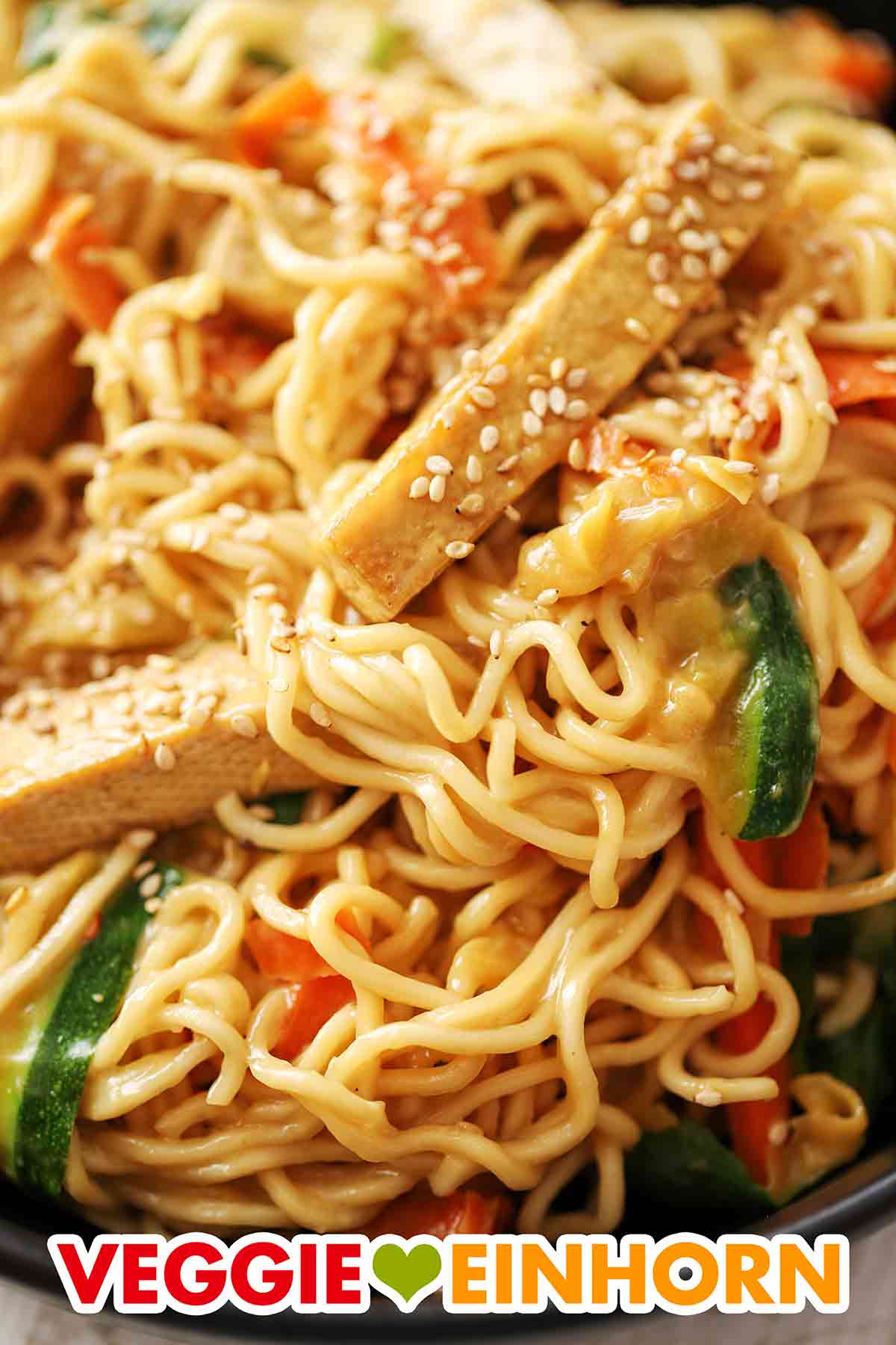 Die Mie Nudeln mit Tofu und Gemüse haben eine leckere Soße aus Mandelmus und Sojasoße. Nahaufnahme von Mie Nudeln mit Tofu, Zucchini, Möhren und Sesam