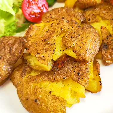 Knusprige smashed Potatoes aus kleinen Drillingkartoffeln mit Schale, goldbraun gebacken, mit Pfeffer gewürzt.