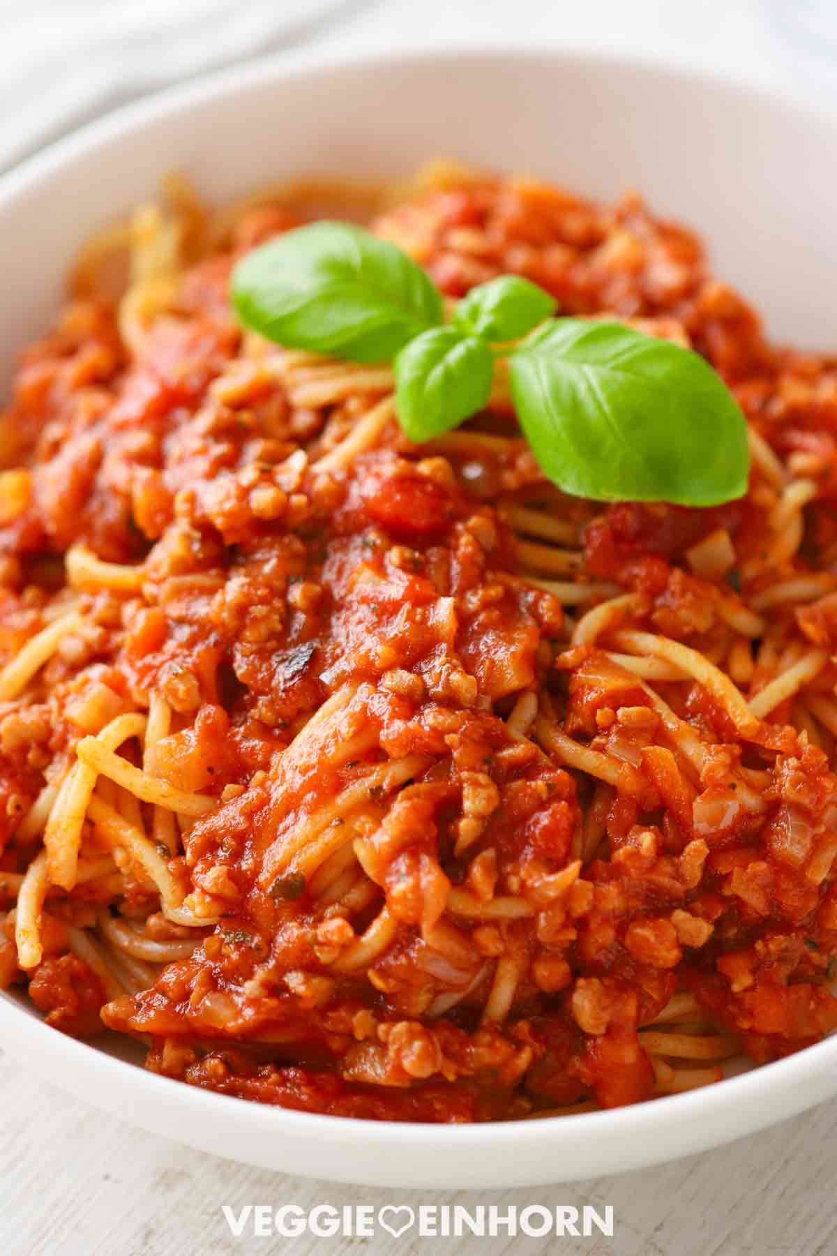 Vegane Bolognese mit Sojagranulat und Spaghetti, angerichtet auf einem weißen Teller, garniert mit frischen Basilikumblättern.
