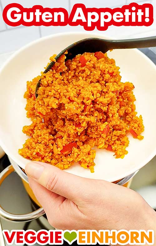 Der Tomatenbulgur ist sehr lecker. Tomaten Bulgur wird mit einem Servierlöffel auf einen Teller gegeben.