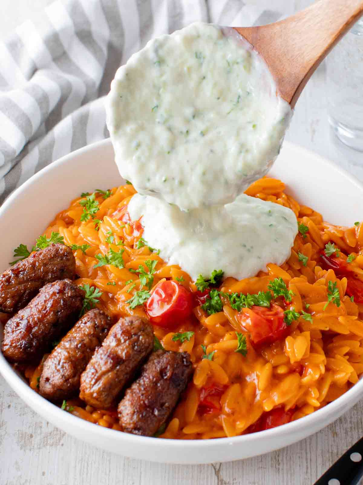 Teller mit Tomaten Kritharaki mit veganem Tzatziki und veganen Cevapcici