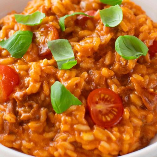 Nahaufnahme von veganem Tomatenrisotto mit Kirschtomaten und frischen Basilikumblättern, serviert in einer weißen Schale.