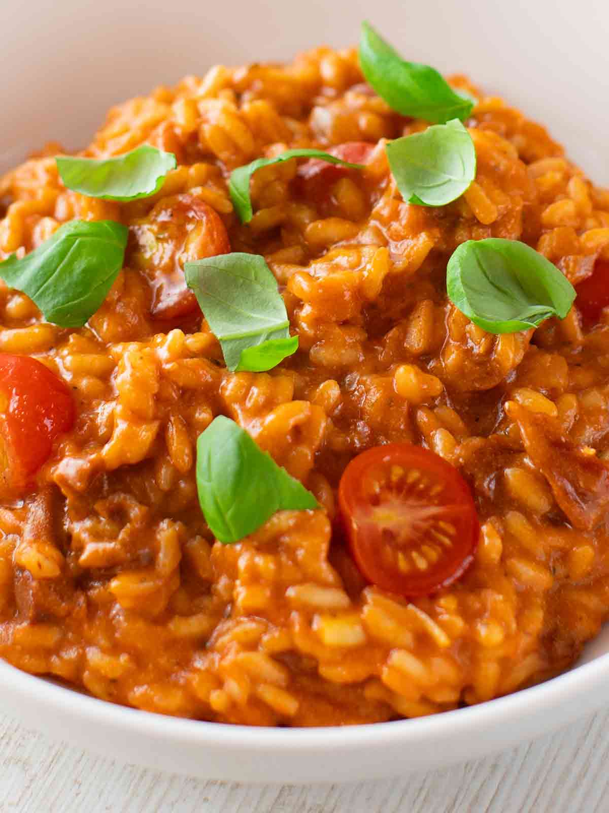 Nahaufnahme von veganem Tomatenrisotto mit Kirschtomaten und frischen Basilikumblättern, serviert in einer weißen Schale.