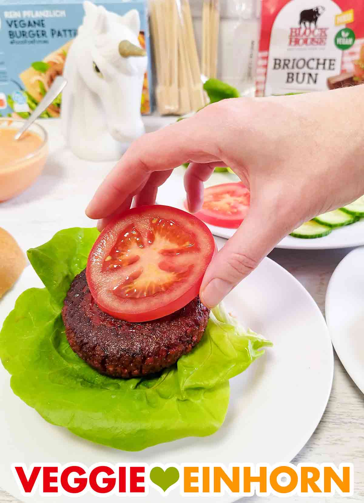 Jetzt kommt eine Scheibe Tomate auf den Burger. Auf den veganen Burger Patty von Penny wird eine Tomatenscheibe gelegt